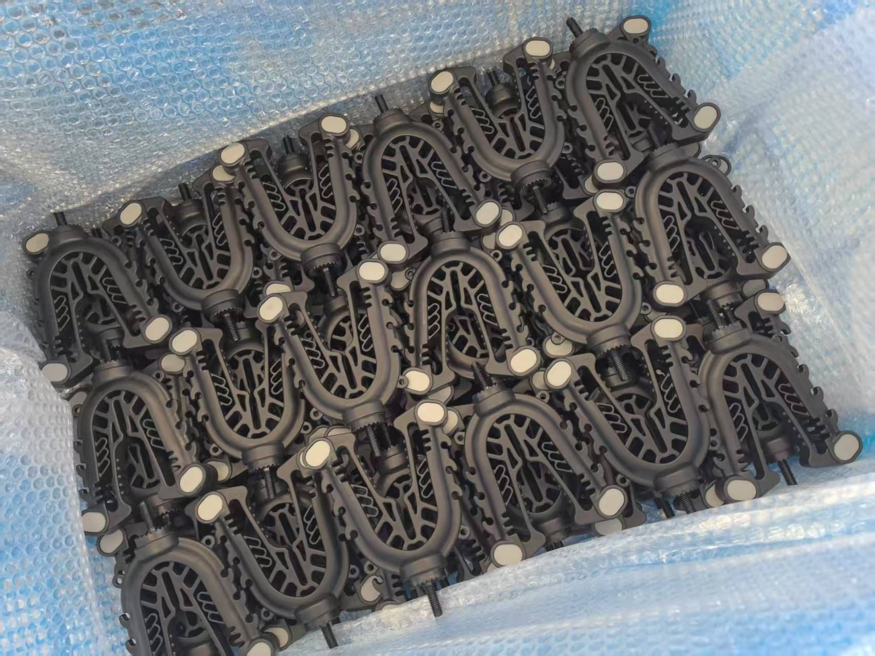 Multiple black clamps with screws packed in bubble wrap inside a box.